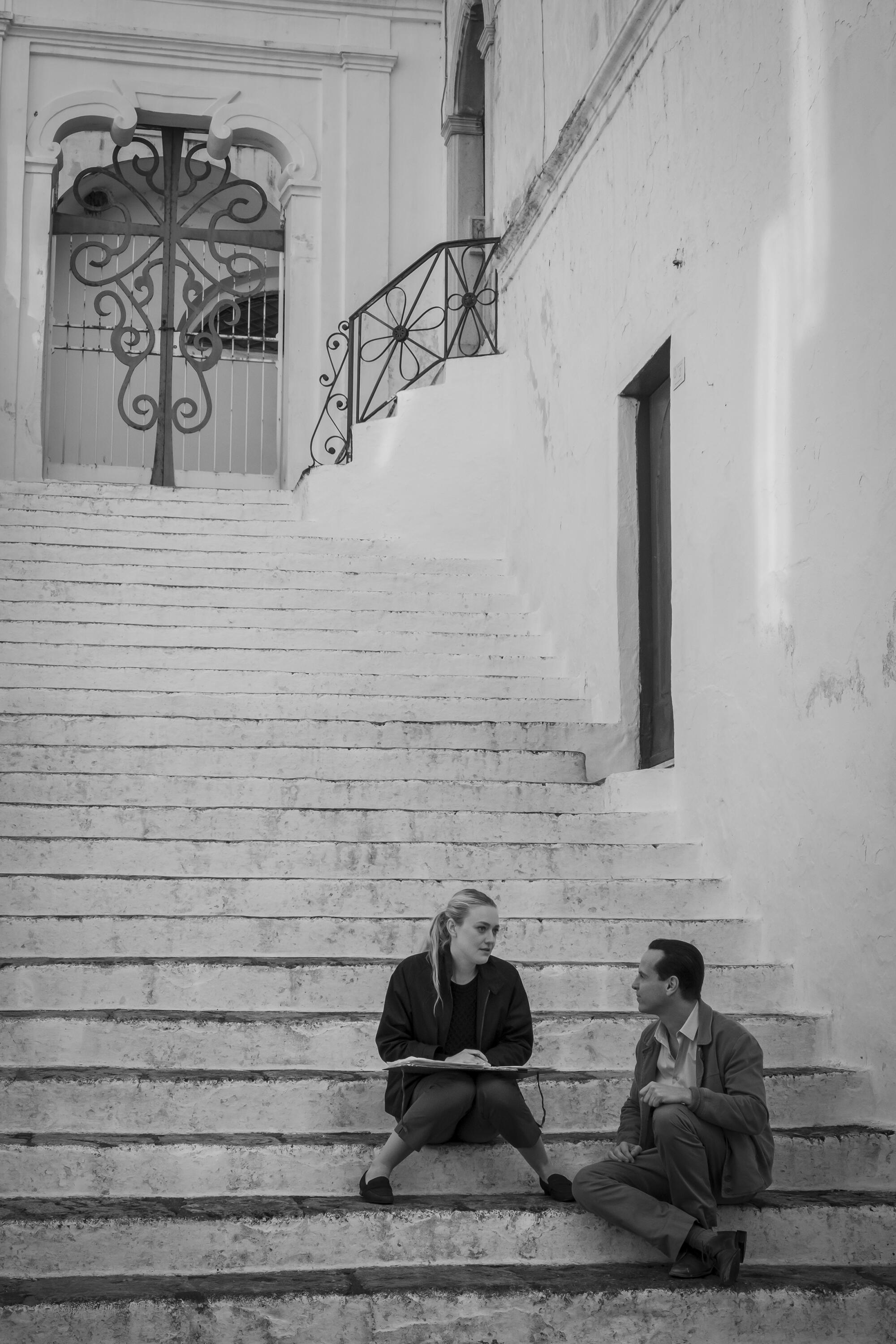 A man and woman sit on outdoor steps in a scene from the black-and-white "Ripley."