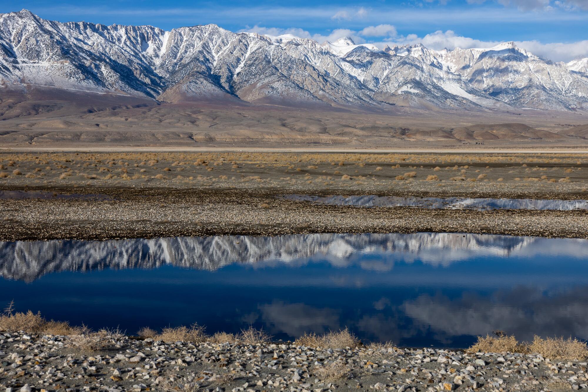 Snow-covered mountains are reflected in a pond