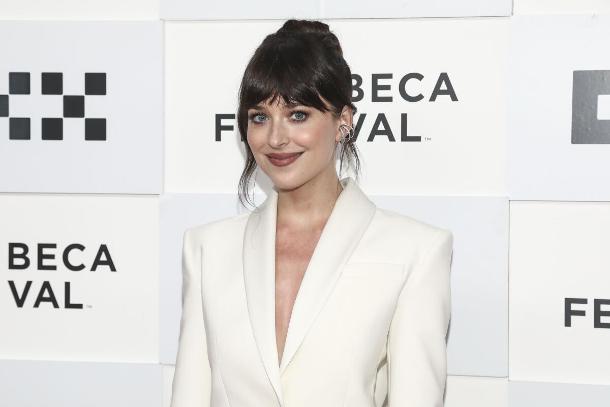 A woman with brown hair and bangs wears a white suit