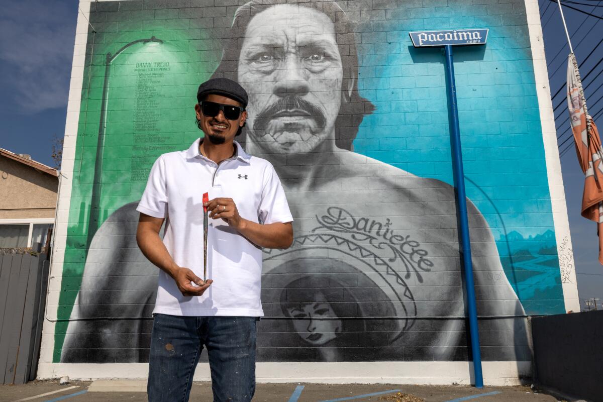 A man stands in front of a mural of another man.