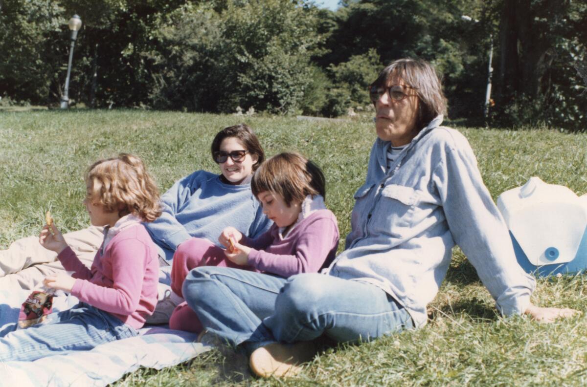 Two moms sit having a picnic in the grass with their toddler daughters in a family photograph from the 1980s. 