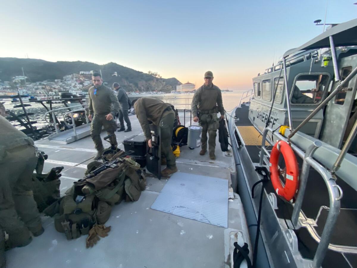 Officers unload gear on a dock next to a boat with the words Los Angeles County Sheriff