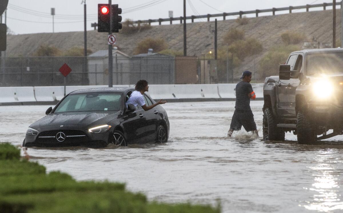 A driver in a half-submerged car asks for help from a passerby during tropical storm Hilary .