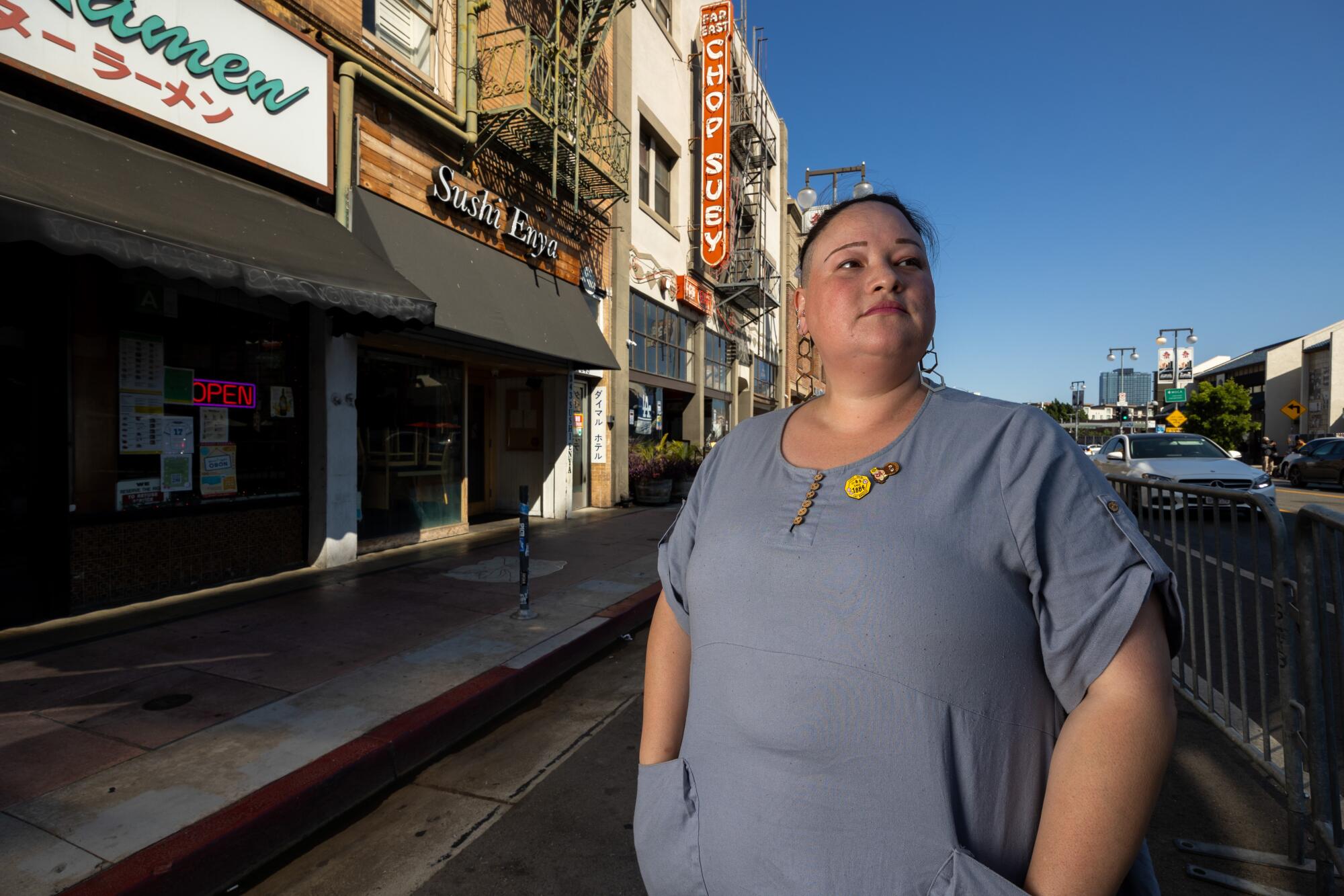 Kristin Fukushima looks to the right while standing on a street of businesses.