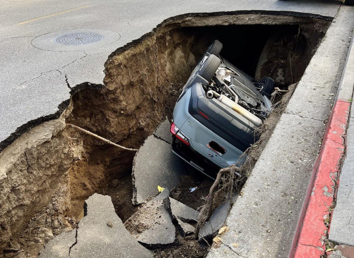 A car is flipped over inside a large sinkhole.