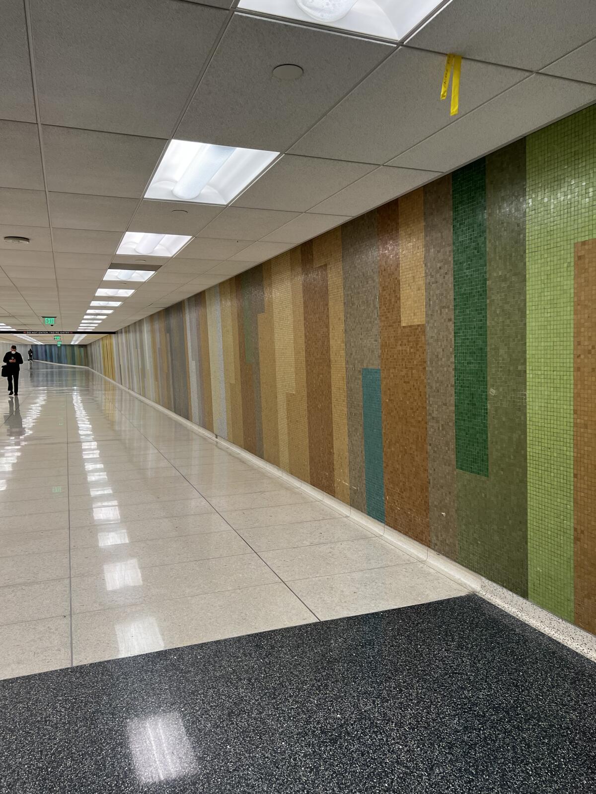 A wall made up of green and brown mosaic tiles in a florescent-lit hallway at LAX