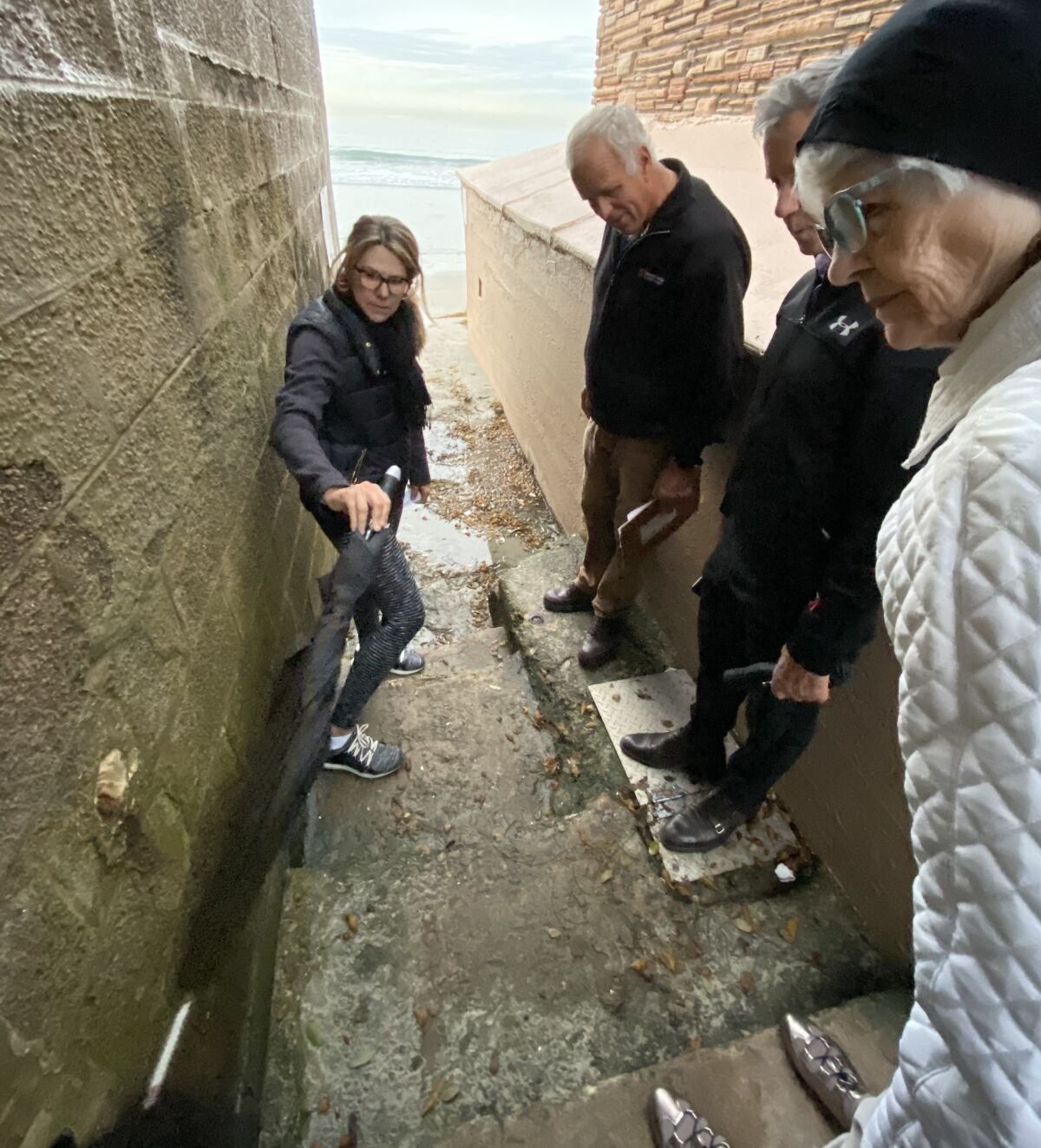 La Jolla resident Jill Peters points with her umbrella at the location for a railing proposed by Members of Friends of the Spindrift Drive Beach Access, a citizens group that also includes Tom Grunow, Patrick Ahern and Dori McCue.