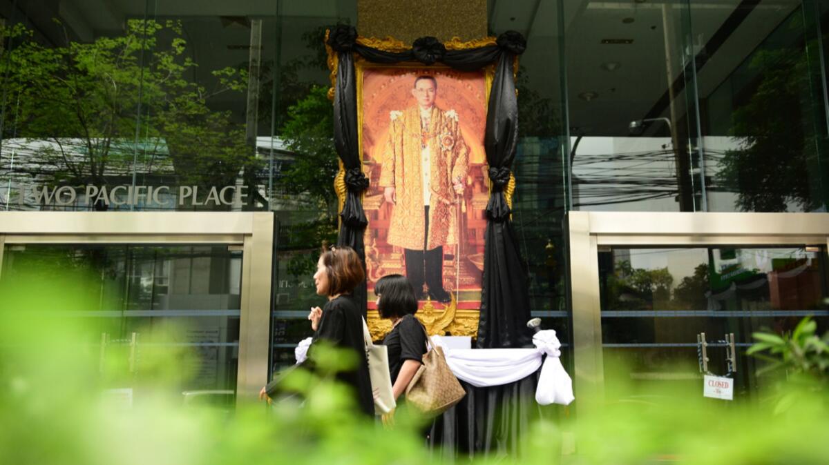 Thais clad in black walk past an image of the late King Bhumibol Adulyadej on one of the main streets in Bangkok on Sunday.