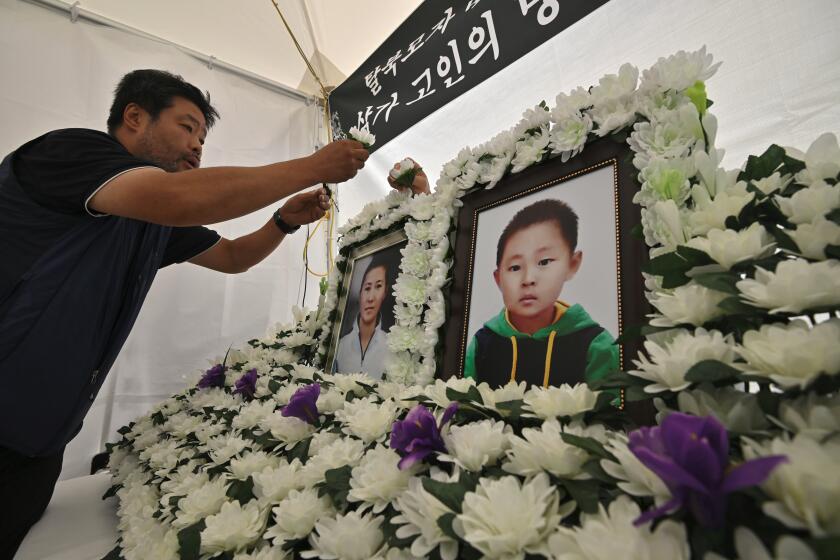 This picture taken on August 28, 2019 shows a man setting up portraits of late North Korean defector Han Sung-ok and her six-year-old son, who are believed to have died from starvation, at a makeshift shrine for Han and her son in downtown Seoul. - Han struggled to hold on to a job while caring for her son and the pair were found two months after their death in their apartment along with an empty bottle of soy sauce. (Photo by Jung Yeon-je / AFP) / TO GO WITH SKorea-NKorea-poverty-social,FOCUS BY Sunghee Hwang (Photo credit should read JUNG YEON-JE/AFP/Getty Images)