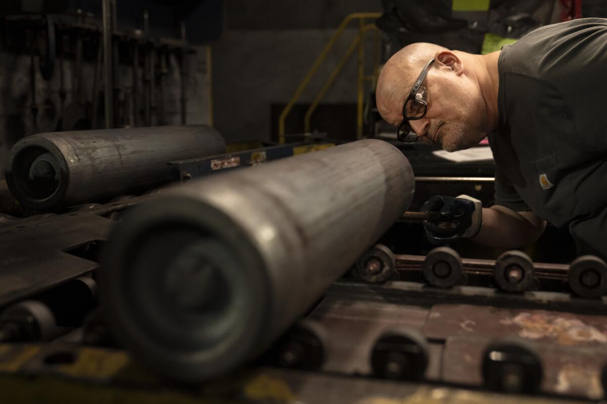 A steel worker inspects an artillery projectile.