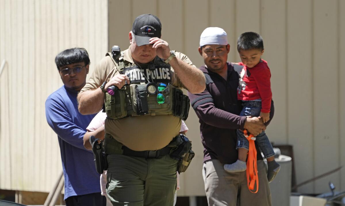 A law enforcement official stands outdoors between two men, one of whom is holding a child. 
