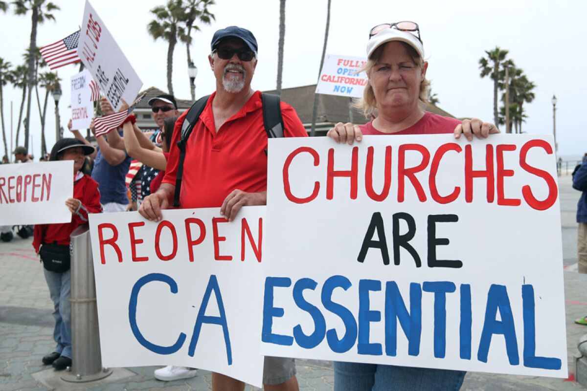 Wally Thomas of Lake Forest and Denean MacAndrew of Mission Viejo take part in a protest in Huntington Beach. More than 1,200 pastors have vowed to hold in-person services on May 31, Pentecost Sunday.