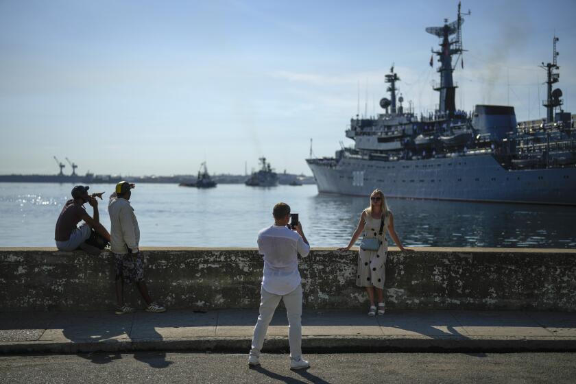 A woman poses for a photo backdropped by the Russian training ship "Smolnyy" as it arrives for a "working visit", in the bay of Havana, Cuba, Saturday, July 27, 2024. (AP Photo/Ramon Espinosa)