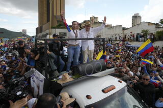 A woman and a man standing in a vehicle, each with one arm raised, amid a sea of people