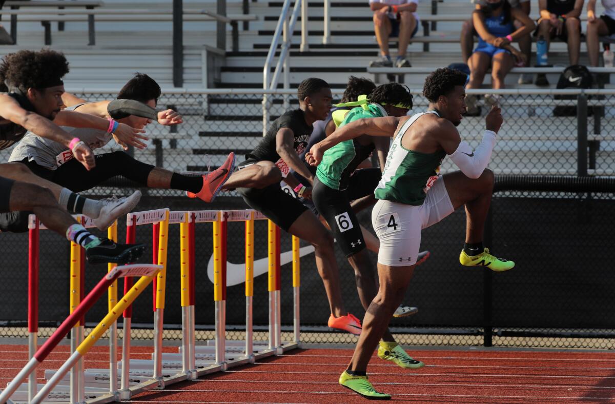 Young men jump over hurdles on a track.