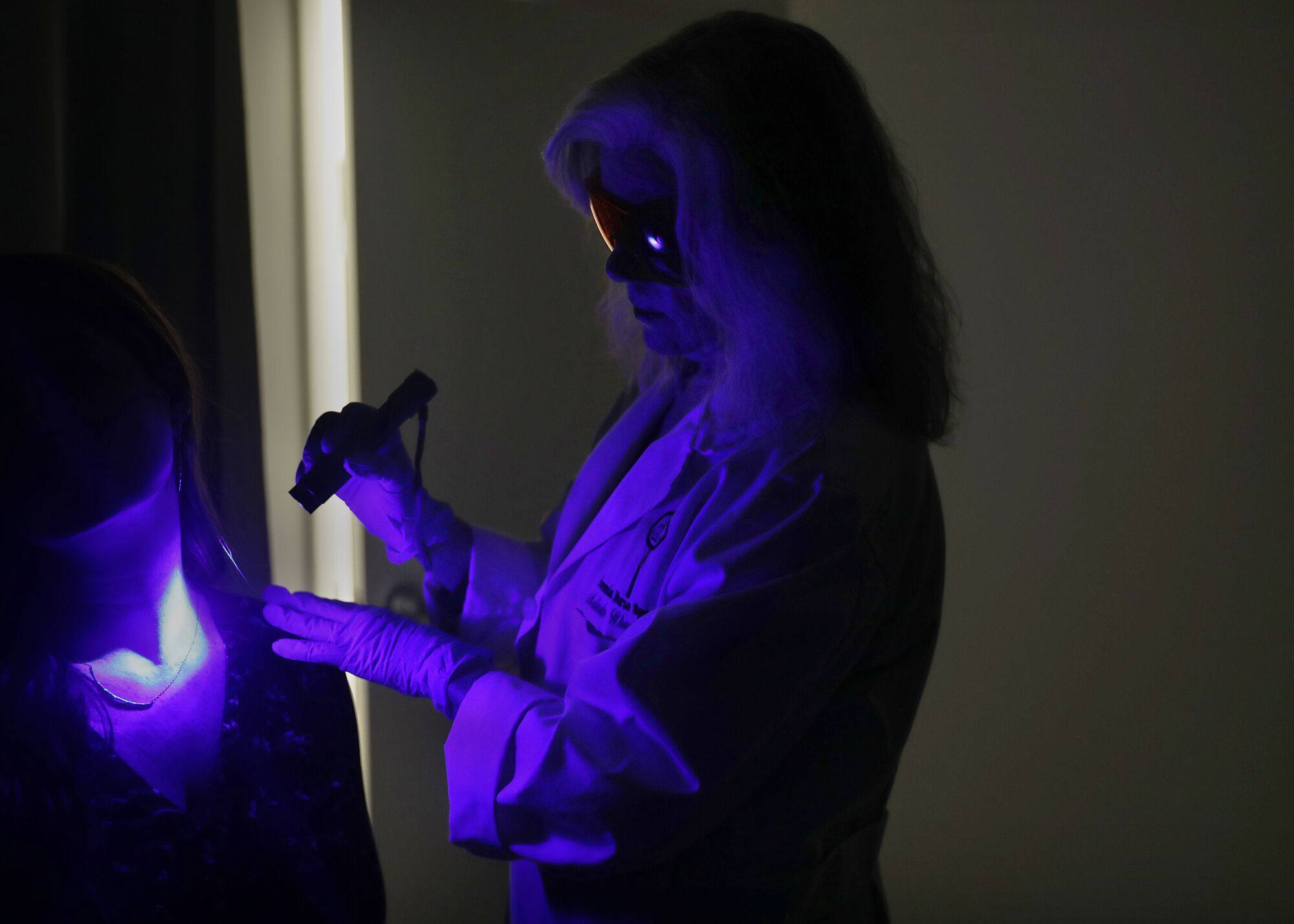 Purple light reflects off a person holding a flashlight-like device in a darkened room.