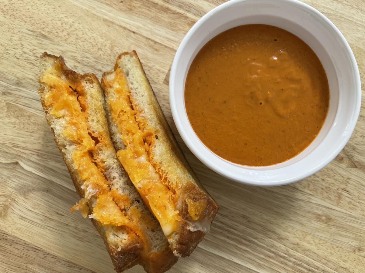 A crisp grilled cheese sandwich beside a cup of tomato soup.