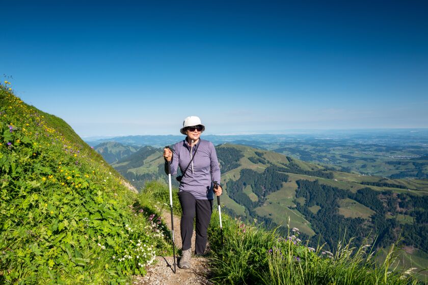 Woman hikes uphill in the mountains during warm weather, using poles for balance. 