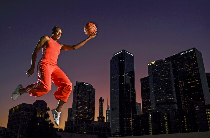 Nneka Ogwumike, holding a basketball, is poised midair against a background of city buildings at sunset.