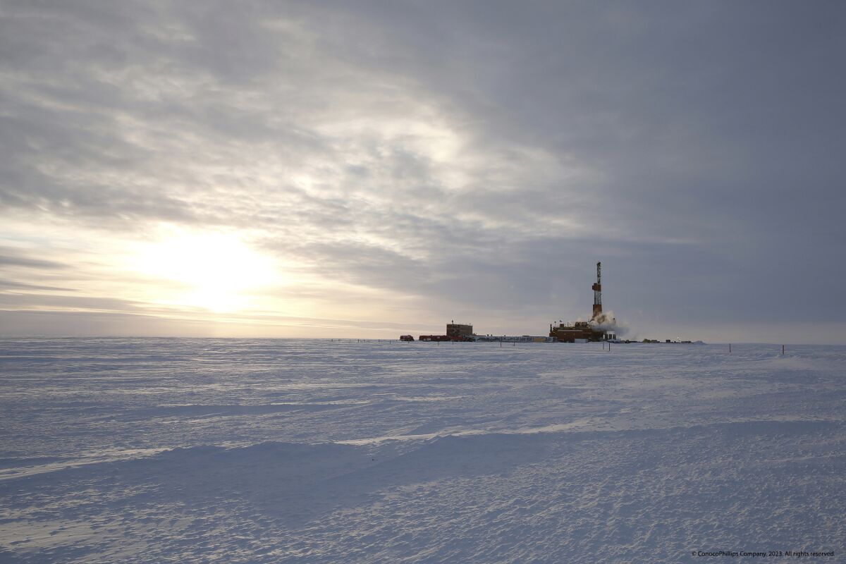 A derrick stands above flat, frozen ground as seen from a distance