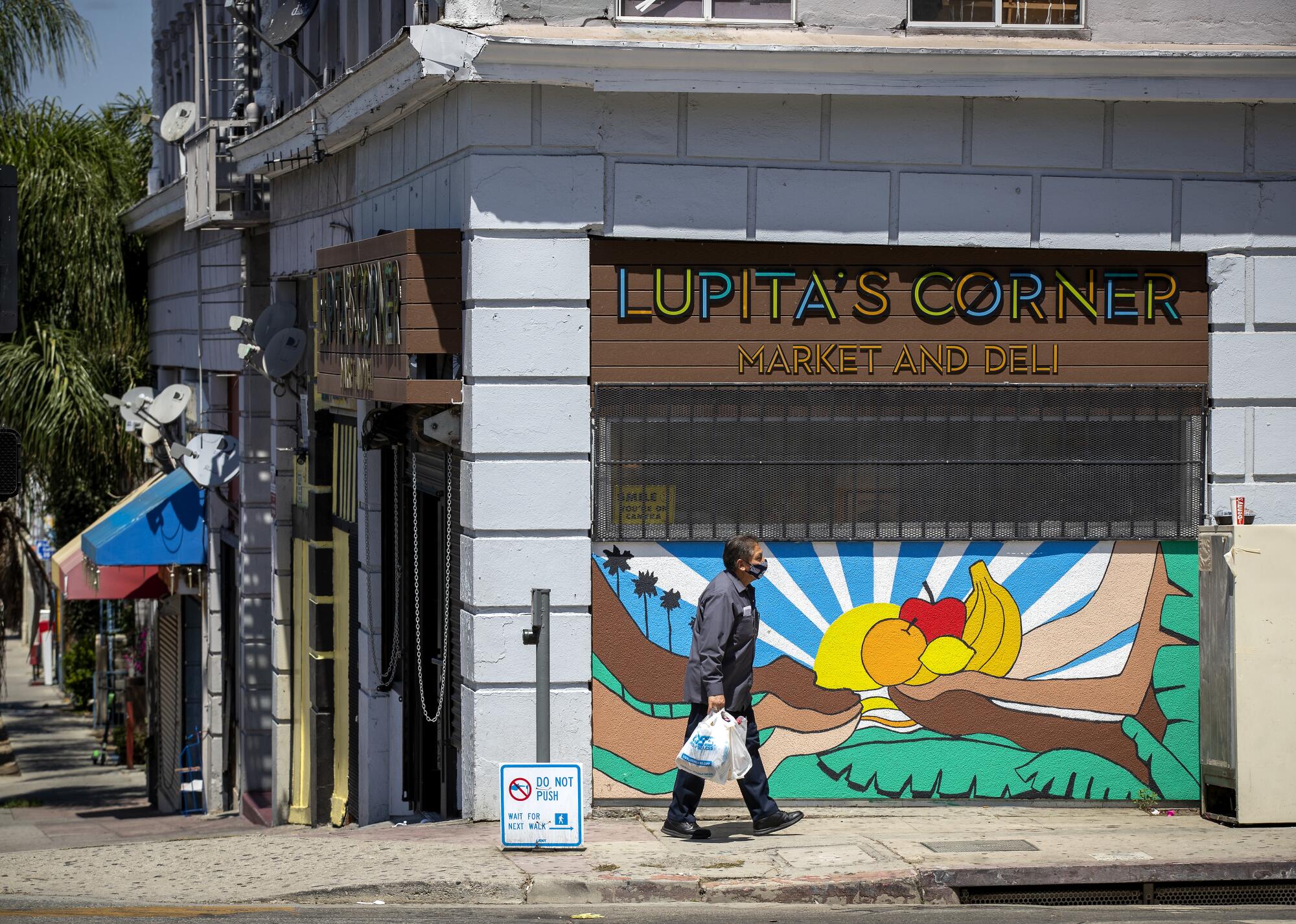 A man carries a bag of food past a mural at Lupita’s Corner Market And Deli