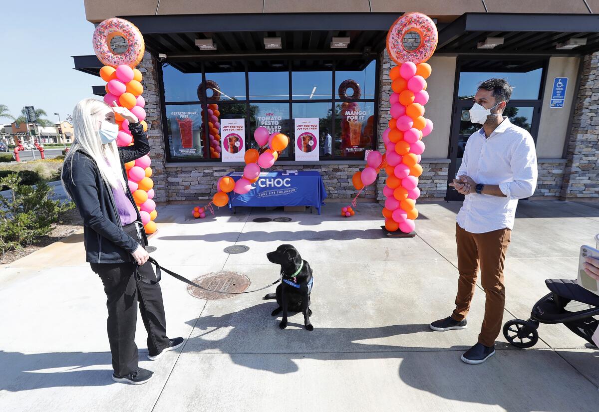 Janessa Vandenberge, CHOC dog handler, black Labrador Odessa and Dunkin' franchise owner Parag Patel.