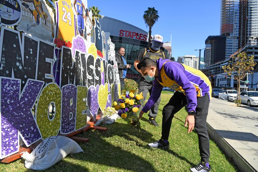 LOS ANGELES, CALIFORNIA JANUARY 26, 2021-Nestor Magana lays places flowers in front of a Kobe Bryant mural on the 1-year anniversary of Kobe Bryant's death in Downtown Los Angeles Tueswday. (Wally Skalij/Los Angeles Times)