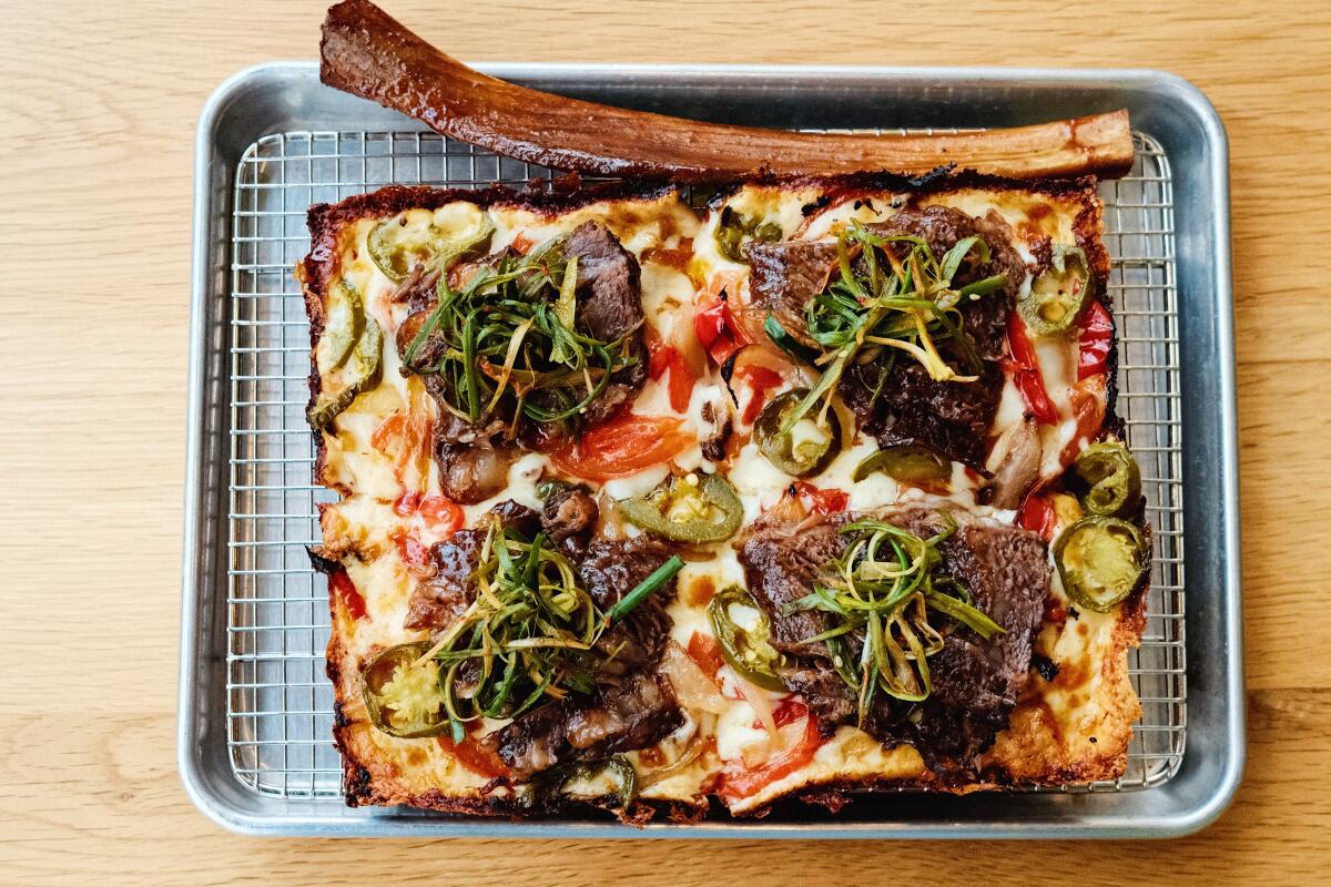 A galbi square pizza on a tray comes garnished with a galbi bone