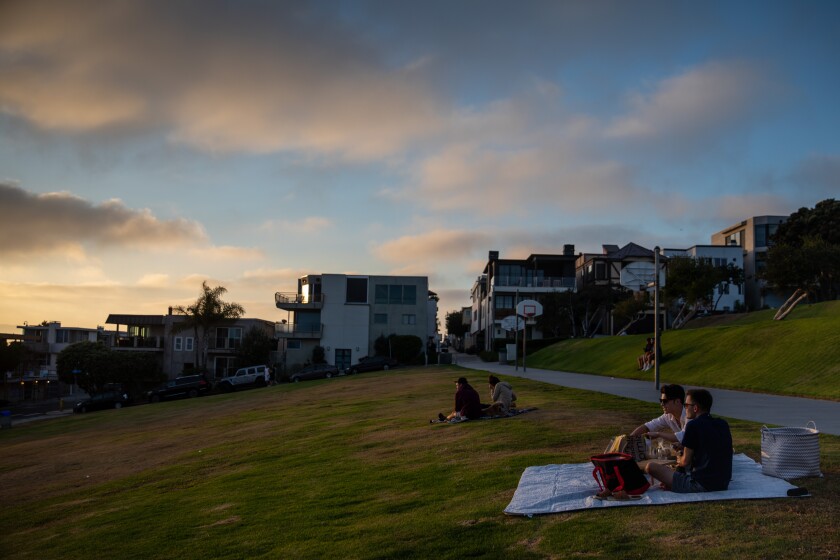 People sit on a grassy slope at sunset.
