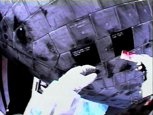 A view from mission specialist Stephen Robinson's helmet on Aug. 3 shows him holding one of two protruding pieces of gap filler that he removed from between two heat shield tiles during the third of three spacewalks.