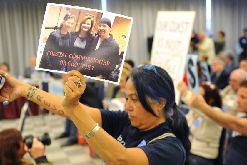 Venice resident Lydia Ponce holds a picture of California Coastal Commissioner Wendy Mitchell, center, standing beside U2 guitarist David "The Edge" Evans at a meeting in Santa Monica.