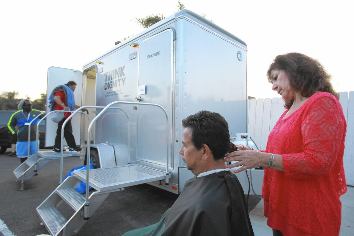 Jose Escoto, who has been homeless for seven months, gets a haircut by volunteer hairstylist Martha Alboney as a man walks into a portable shower in Chula Vista.