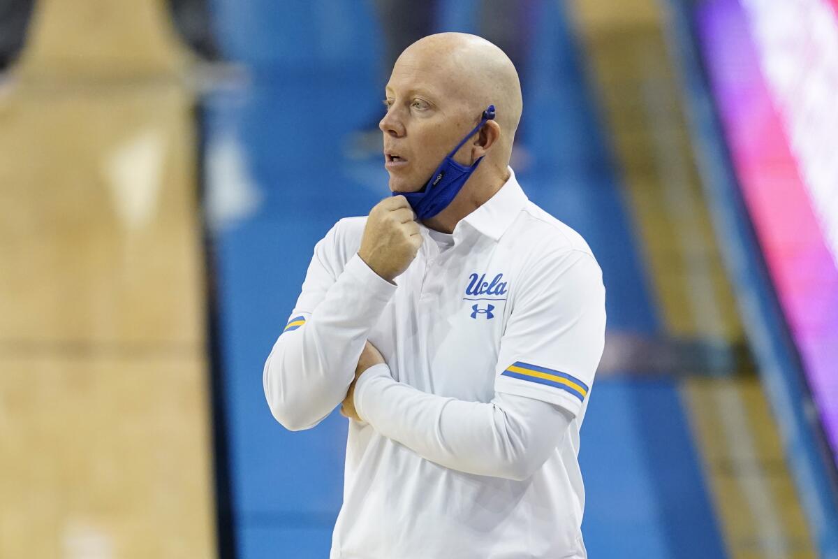 UCLA coach Mick Cronin adjusts his mask on the sideline.