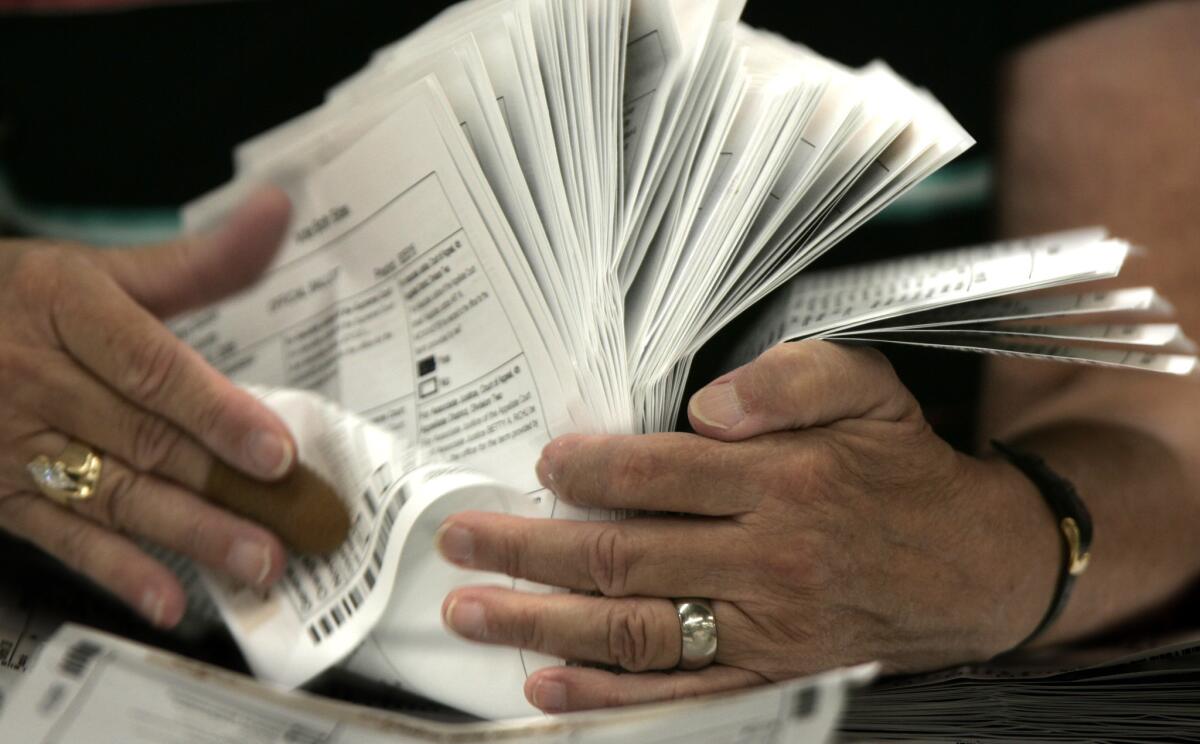 An election worker in Santa Ana with a stack of absentee ballots. A new California state law will shift millions more voters to casting ballots by mail as soon as next year.