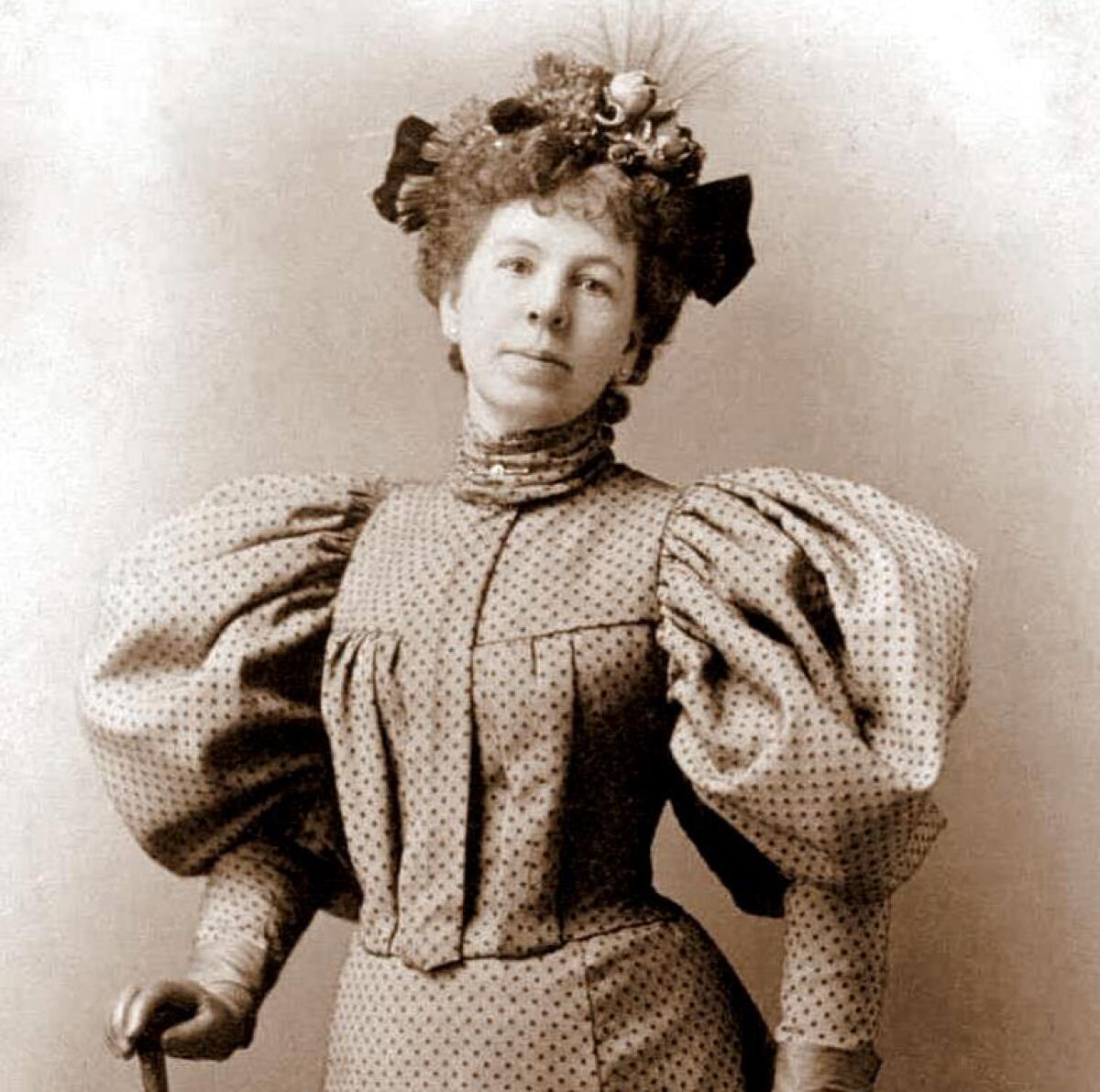 A woman poses for a photo wearing a small hat with a fake bird and a dress with mutton-chop sleeves and high neck.