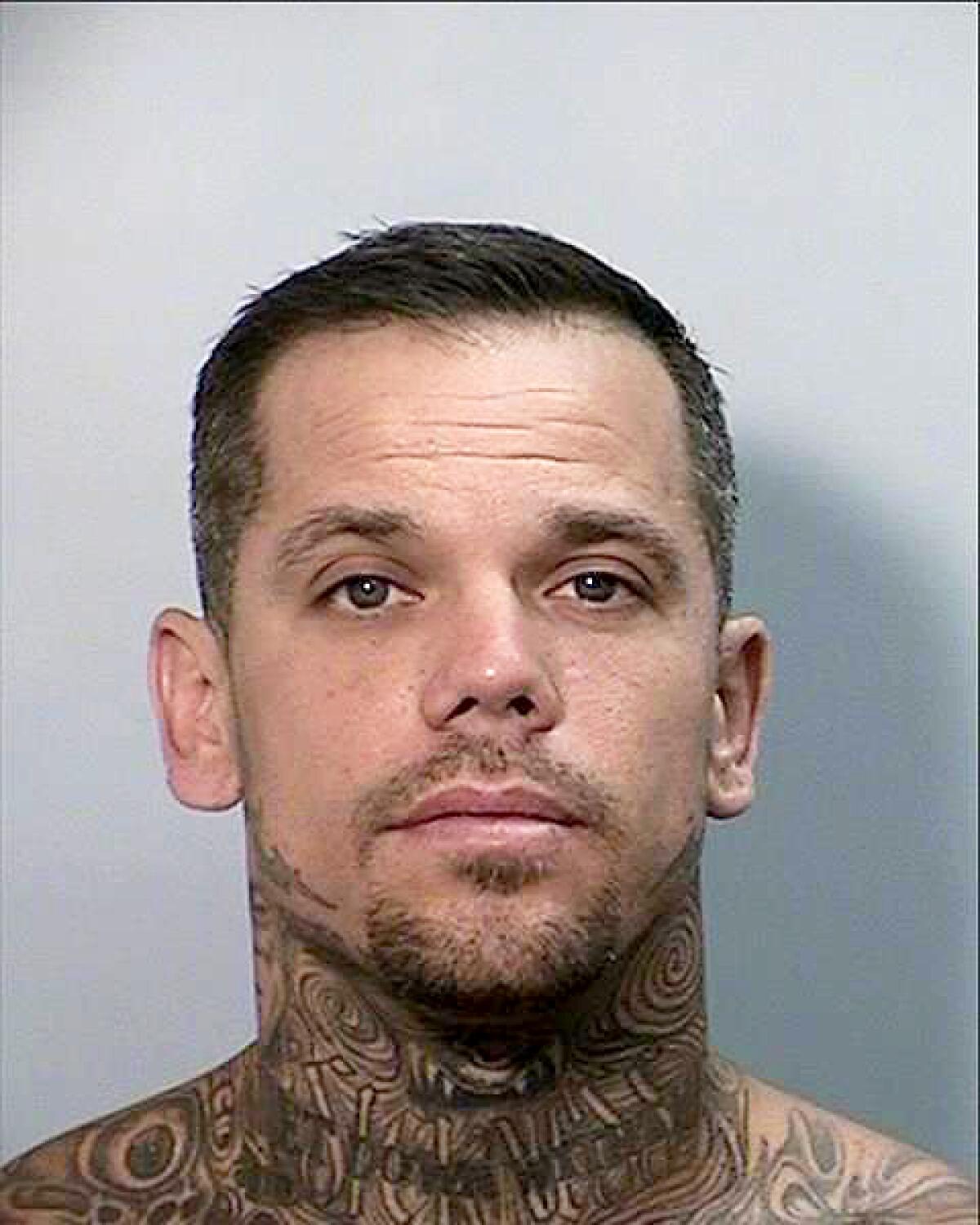 A mug shot of a man with facial hair and neck tattoos. 