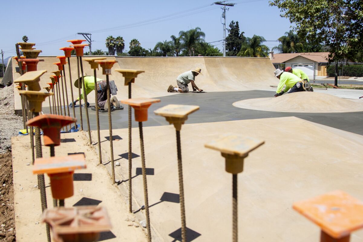 Construction workers smooth out concrete at a site for a new skate park being built at Washington Park in Escondido , CA.