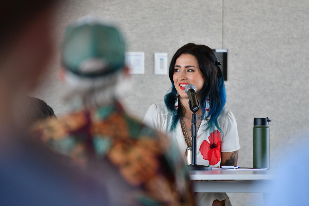 A woman seated at a table speaks to an audience