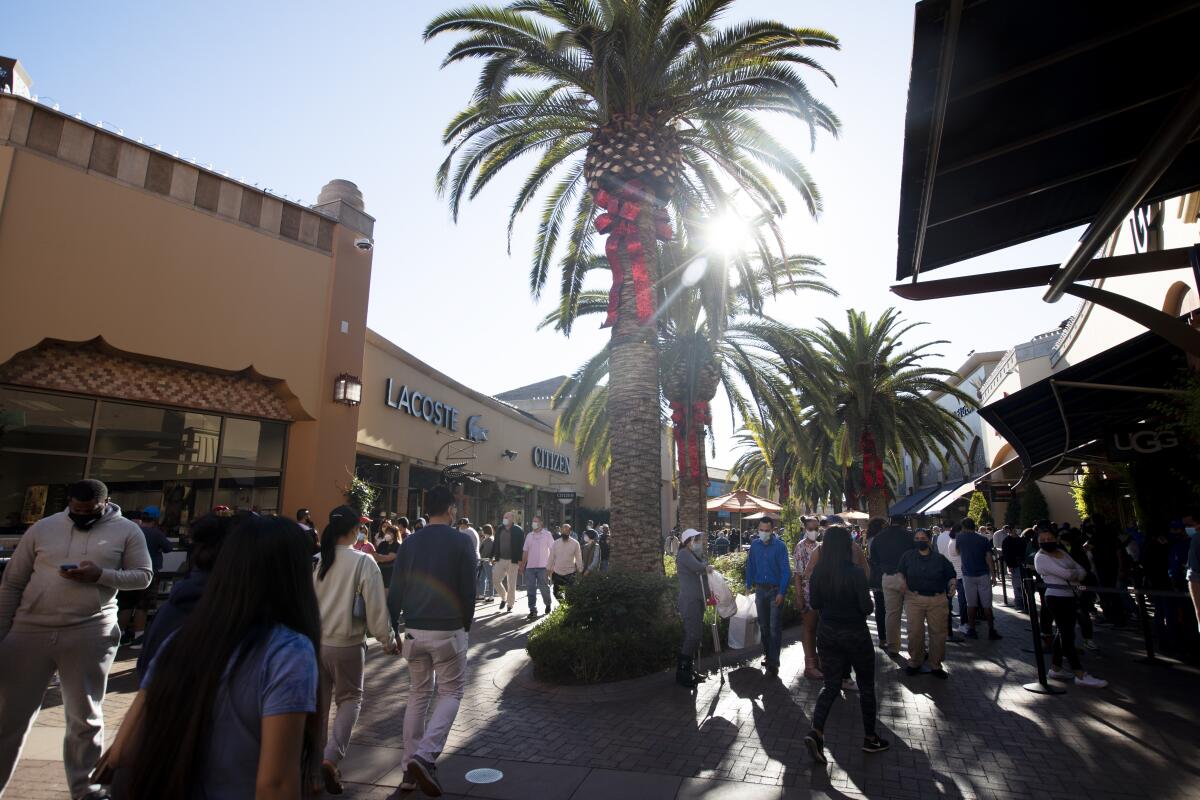 A crowd of shoppers beneath palm trees at an outdoor mall.