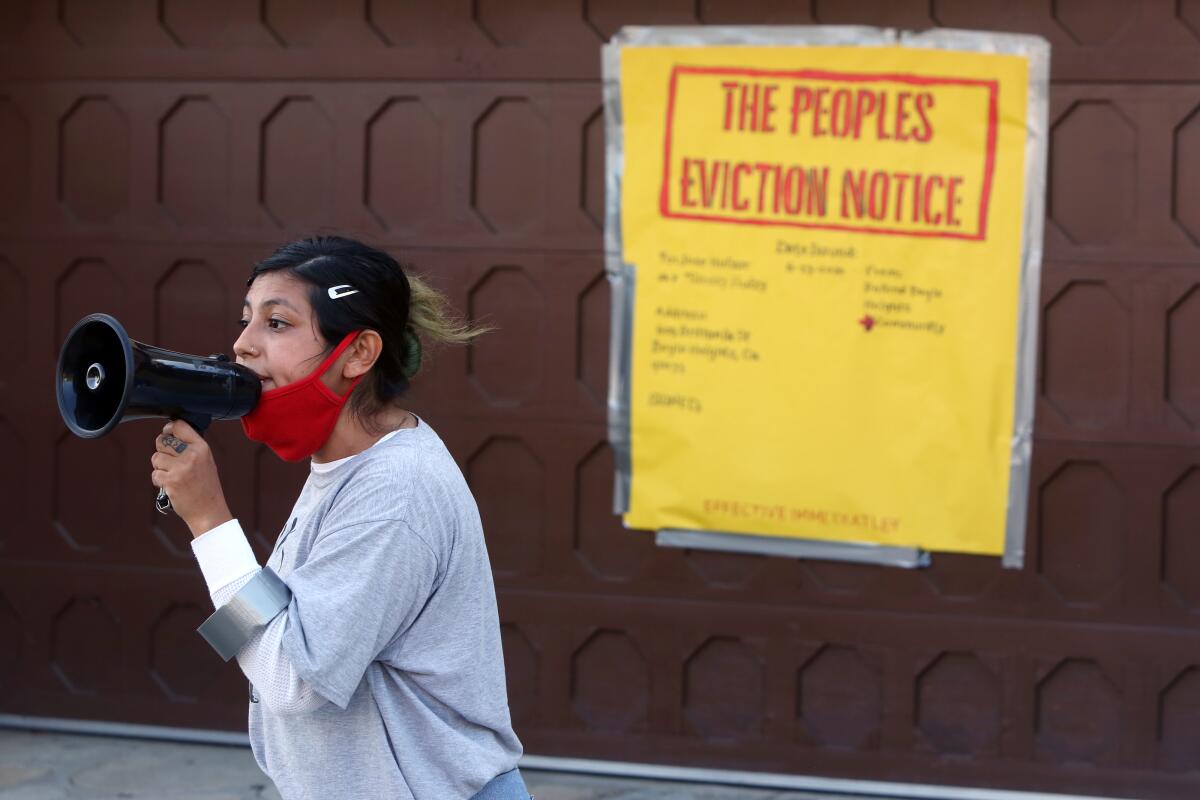A woman speaks into a megaphone in front of a yellow poster reading "The Peoples Eviction Notice."