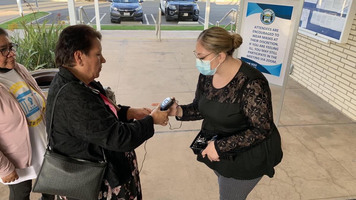 A Costa Mesa staffer, right, offers a translation device to a Spanish-speaking resident ahead of a June 21 Council meeting.
