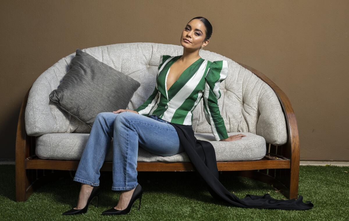 Vanessa Hudgens sits on a chair while wearing a striped shirt and blue jeans