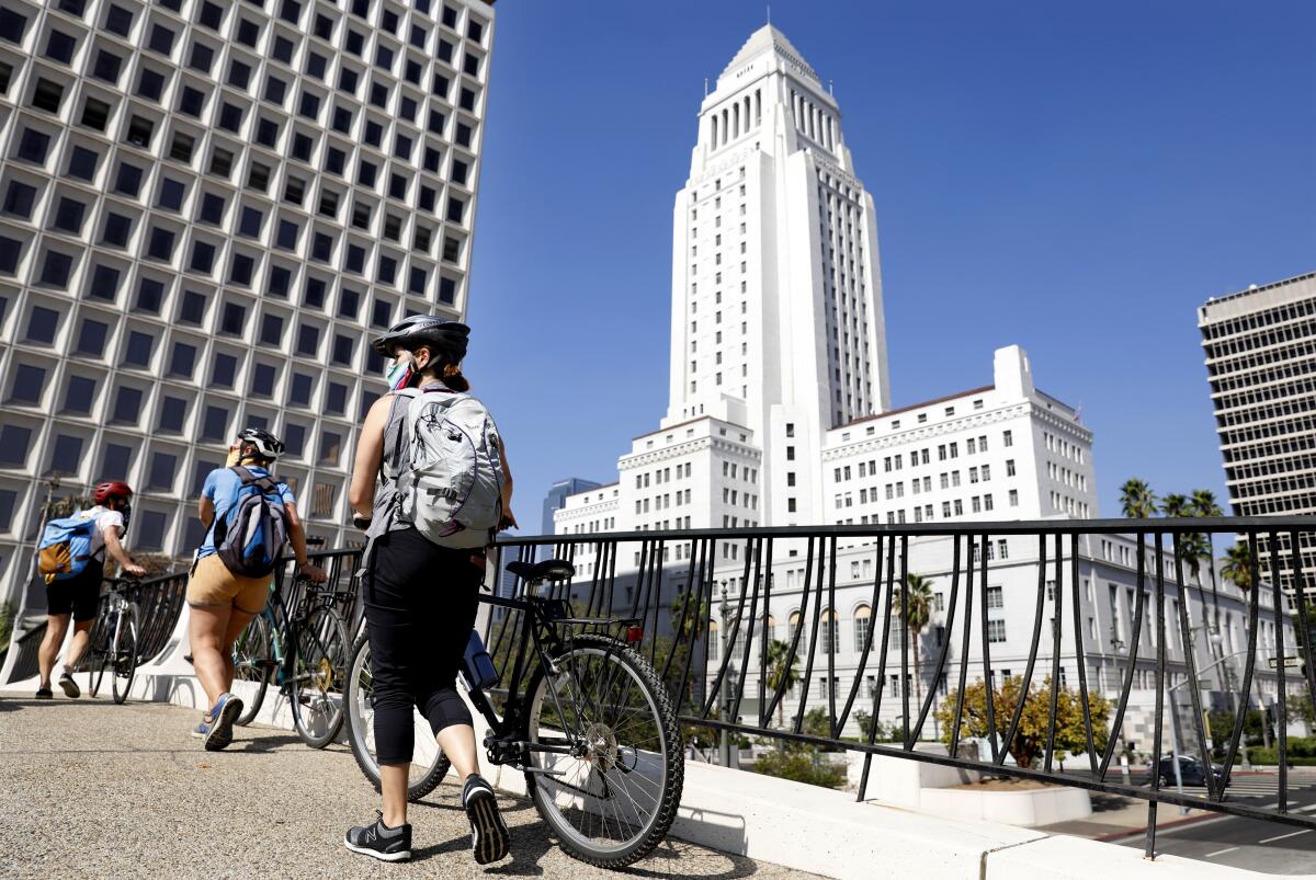 From left, Aimee Gilchrist, Marissa López, and Yvonne Condes, walk their bikes through downtown Los Angeles 