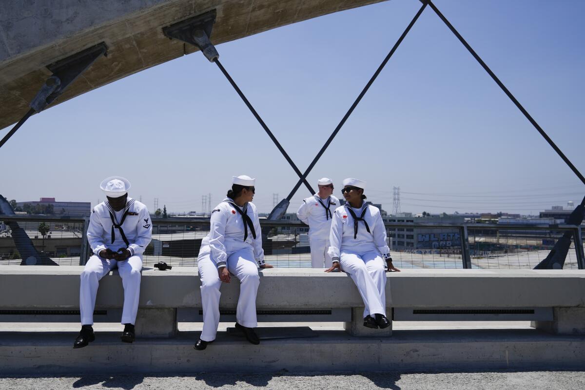Some people in white uniforms are sitting on a concrete barrier.