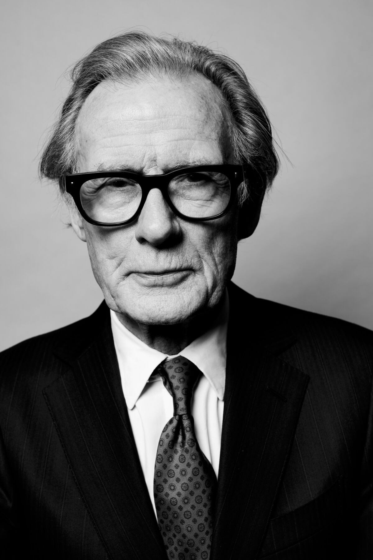 A black-and-white portrait of a man in a dark suit and glasses