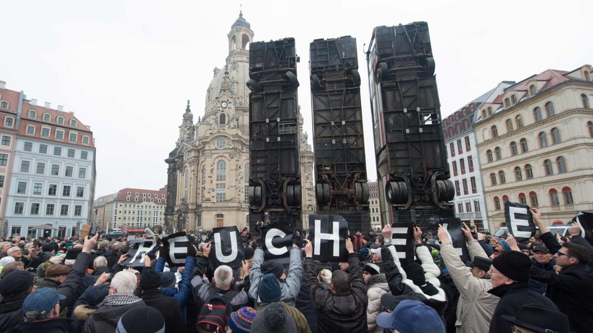 Demonstrators hold up posters reading "hypocrisy" before an installation of upturned buses by Syrian-born artist Manaf Halbouni in Dresden