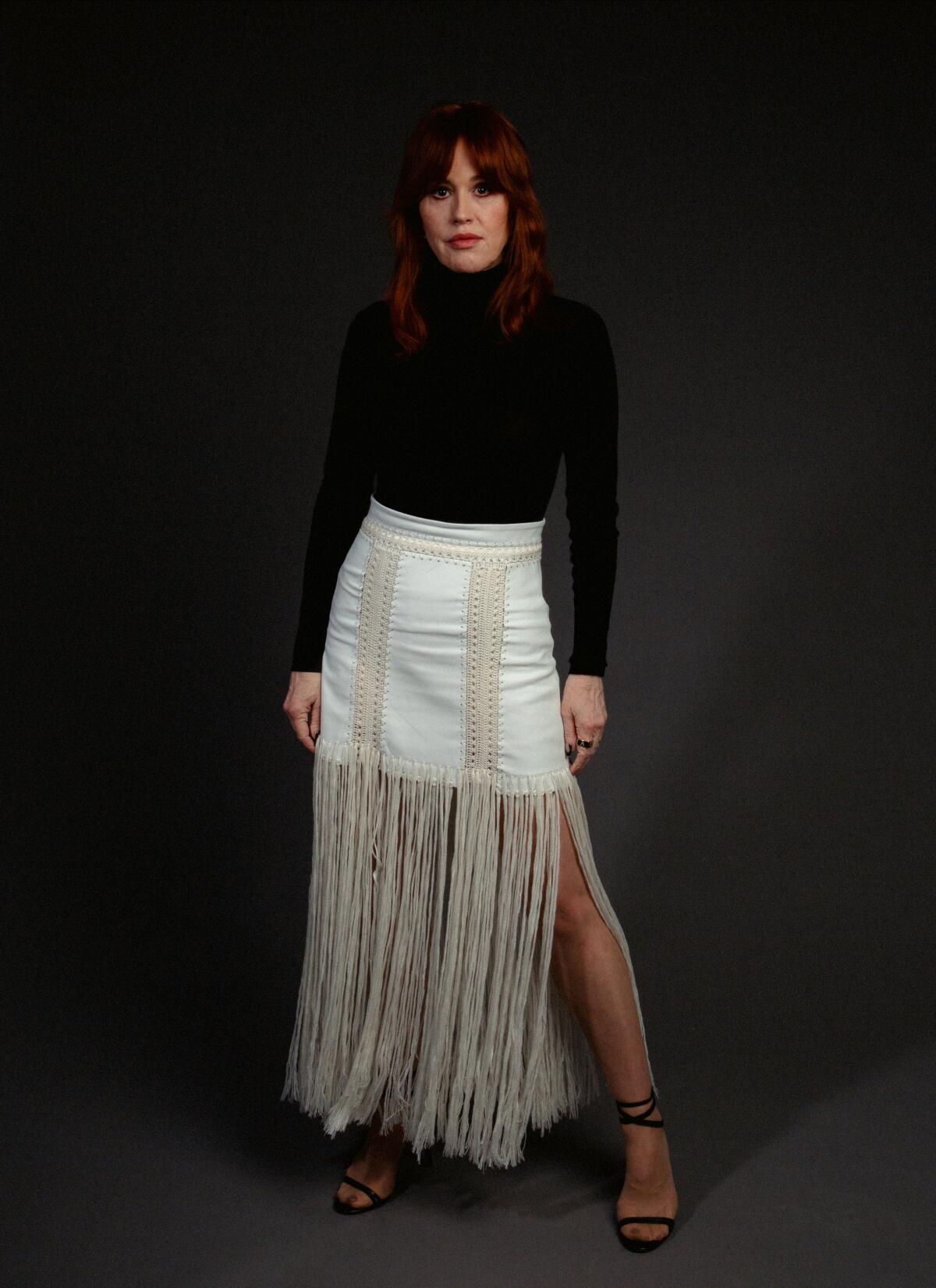 Molly Ringwald in black turtleneck and white skirt.