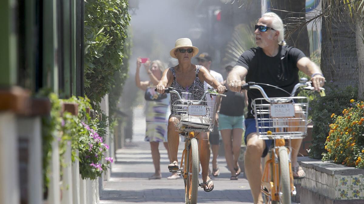 Visitors on their bikes pass under cool mist in Palm Springs on June 20, 2017, a day on which the temperature reached 122 degrees.