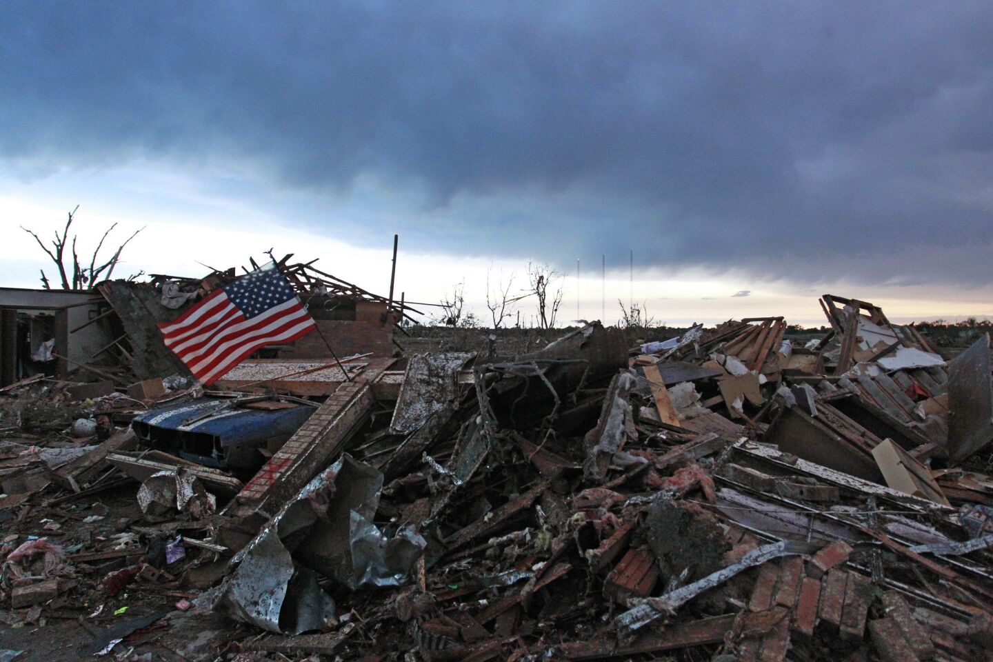An American flag blows in the wind at sunrise atop the rubble of a destroyed home a day after a tornado moved through Moore, Okla.