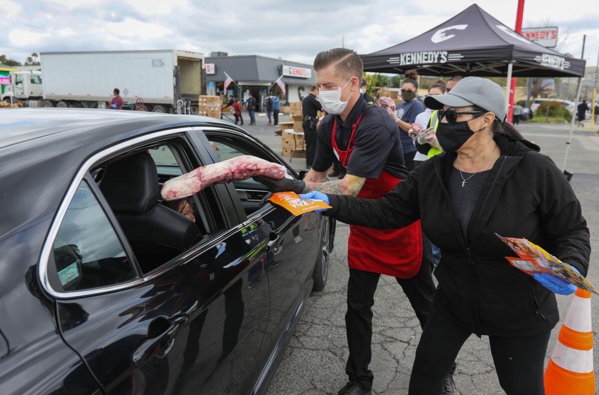 Cody Hathaway and Joann Barnette place large packages of meat and beef jerky in the rear side window of one of the many vehicles passing through the parking lot of Kennedy's Meat Company on East Valley Parkway in Escondido. Over 20,000 pounds of meat was given away.